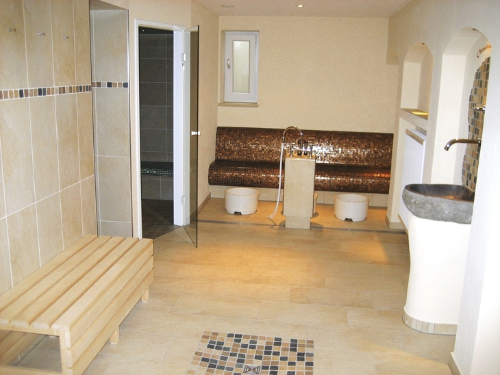 Innenraum einer Sauna mit Holzbänken und Fliesenwänden.