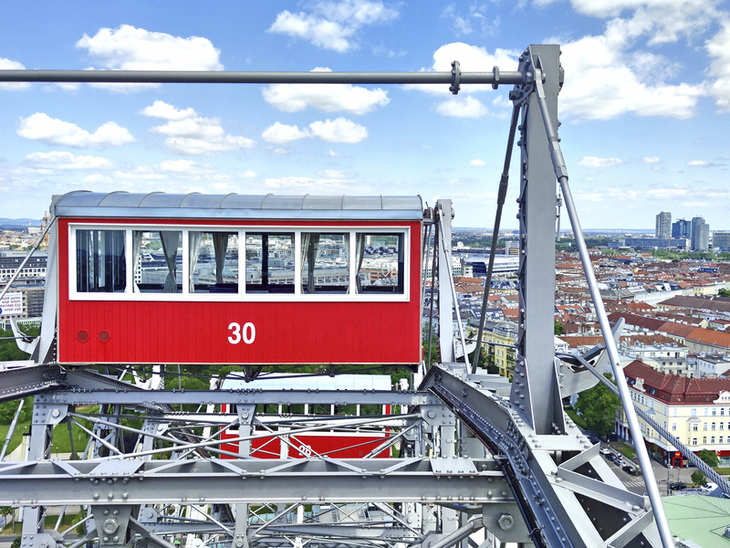 Rotes Riesenrad-Gondel überblickt Stadtlandschaft mit blauem Himmel.