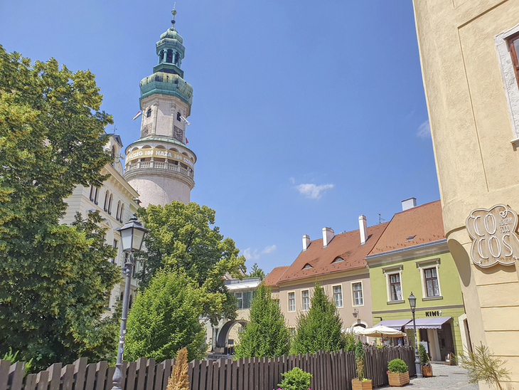 Feuerwachturm in Sopron vor blauem Himmel und umliegenden Gebäuden.