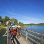 Radfahrer auf Holzbrücke am Chiemsee bei sonnigem Wetter.