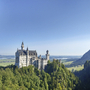 Schloss Neuschwanstein auf einem Hügel, umgeben von Wald und Bergen im Hintergrund.