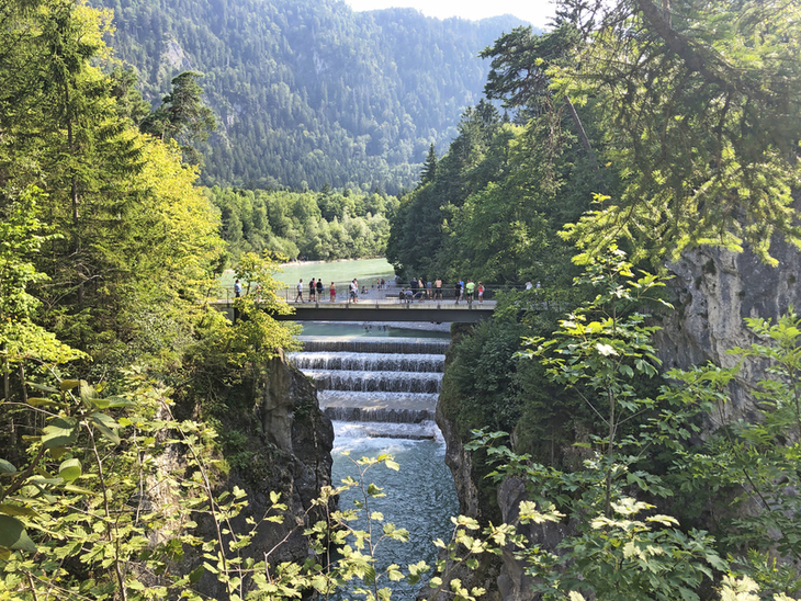 Aussicht auf den Lechfall mit Wanderern auf einer Brücke, umgeben von Wald und Bergen.
