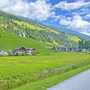 Landschaft mit Radweg, grünen Wiesen, Dorf und Kirche in den Alpen