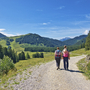 Paar wandert auf einem Weg in einer alpinen Landschaft bei sonnigem Wetter.