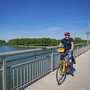 Radfahrer auf einer Brücke am Rhein bei sonnigem Wetter.