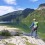 Wanderer mit Rucksack steht am Ufer des Wolfgangsees und blickt auf die Berge.