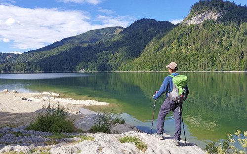 Wanderer mit Rucksack steht am Ufer des Wolfgangsees und blickt auf die Berge.