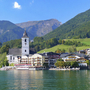 Kirche und Gebäude am Ufer des Wolfgangsees, umgeben von Bergen.