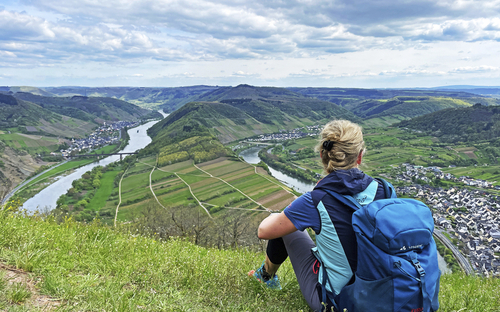 Wanderer mit Rucksack blickt auf Mosellandschaft von einem Hügel.