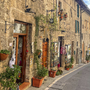 Schmale gepflasterte Gasse in Assisi mit historischen Steinhäusern und Blumendekorationen.