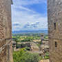 Blick durch enge Gasse auf grünes Tal und Himmel in Umbrien, Italien.