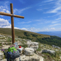 Holzkreuz auf einem Hügel mit Wanderausrüstung im Vordergrund und weiter Aussicht.