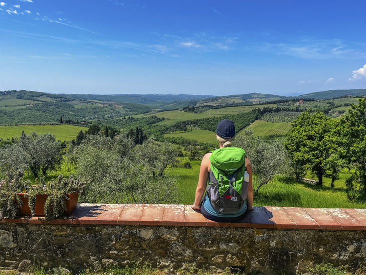 Person sitzt auf Mauer und blickt auf grüne, hügelige Landschaft in Umbrien.