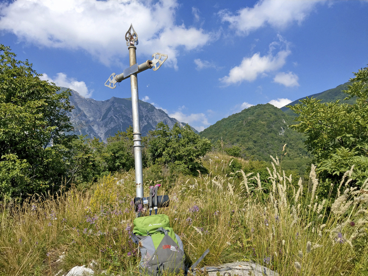 Kreuz auf Wiese mit Bergen und blauem Himmel im Hintergrund