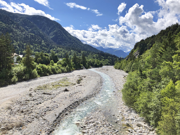 Flussbett mit bewaldeten Bergen und blauem Himmel im Hintergrund