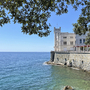Schloss an der Küste mit Blick auf das Meer und umgeben von grünen Bäumen.