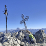 Person mit Rucksack am Gipfelkreuz auf der Cima del Cacciatore in den Julischen Alpen.