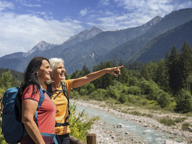 Zwei Wanderer am Flussufer in den Julischen Alpen, eine Person zeigt in die Ferne.
