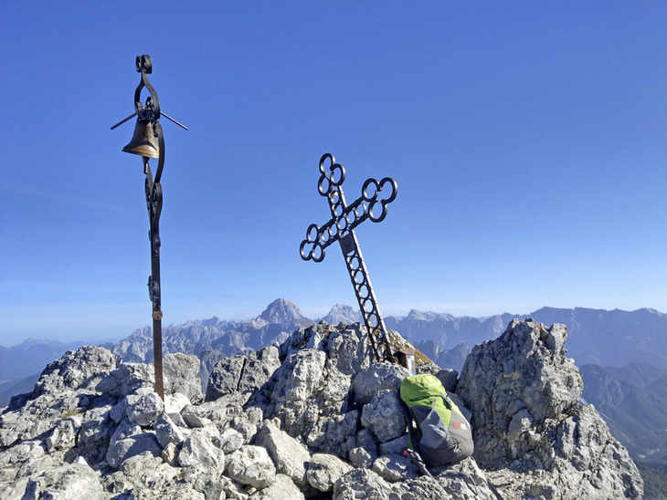 Gipfelkreuz auf felsigem Berggipfel mit Rucksack im Vordergrund