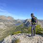 Wanderer mit Rucksack blickt auf Berglandschaft mit Seen und blauem Himmel.