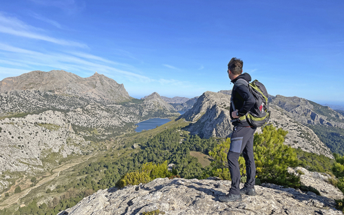 Wanderer mit Rucksack blickt auf Berglandschaft mit Seen und blauem Himmel.