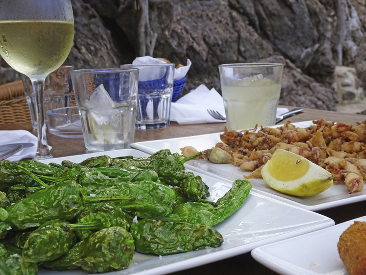 Tapas-Gericht auf einem Tisch mit Getränken und Felsen im Hintergrund.