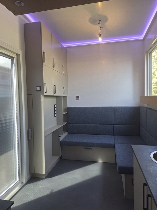 Innenansicht eines modernen Tiny Houses mit Sitzgelegenheiten und violetter Beleuchtung.