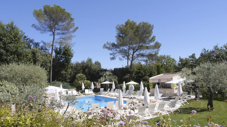 Hotel-Poolbereich mit Liegen und Sonnenschirmen, umgeben von Bäumen und Pflanzen.