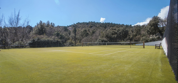 Tennisplatz im Freien umgeben von Bäumen und Hügeln bei klarem Himmel.