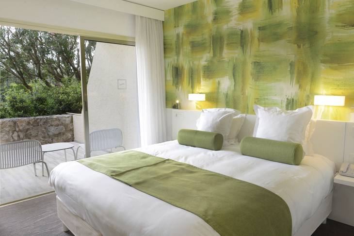 Helles Hotelzimmer mit Doppelbett und grünem Wanddesign, Blick auf Terrasse.