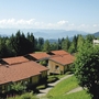 Häuser mit roten Dächern vor Alpenpanorama und bewaldeter Landschaft.