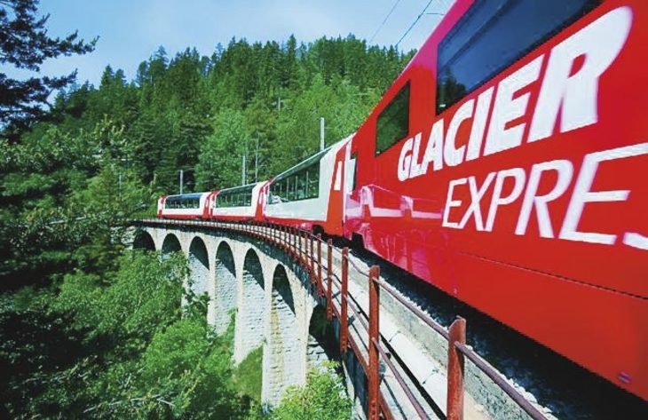 Zug des Glacier Express auf einem Viadukt in einer Alpenlandschaft.