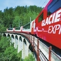 Zug des Glacier Express auf einem Viadukt in einer Alpenlandschaft.