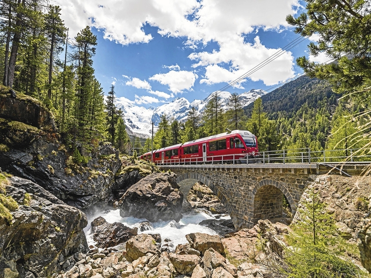 Roter Zug der Bernina Bahn fährt über eine steinerne Brücke in bergiger Landschaft.