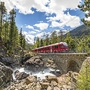Roter Zug der Bernina Bahn fährt über eine steinerne Brücke in bergiger Landschaft.
