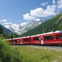Roter Zug der Bernina Bahn vor Bergkulisse und Wolken am Himmel.