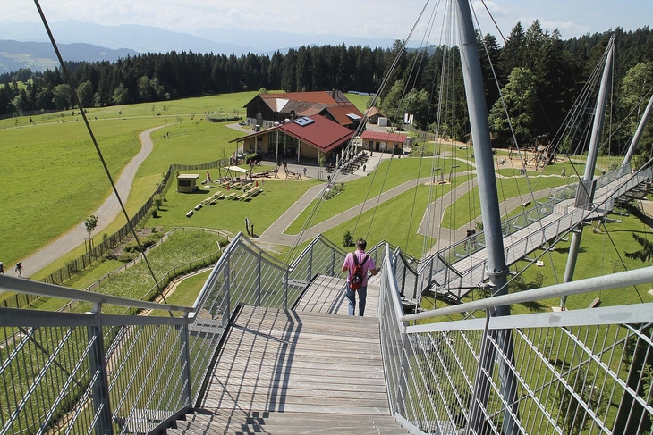 Person geht über Skywalk in Scheidegg mit Blick auf Wiesen und Gebäude.