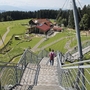 Person geht über Skywalk in Scheidegg mit Blick auf Wiesen und Gebäude.