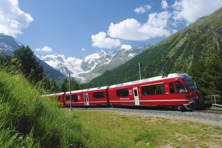 Roter Zug der Bernina Bahn vor Bergkulisse und Wolken am Himmel.