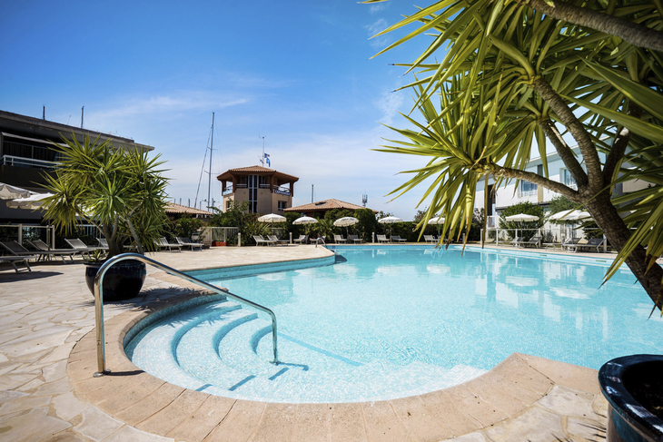 Poolbereich eines Hotels mit Liegestühlen und Palmen bei sonnigem Wetter.