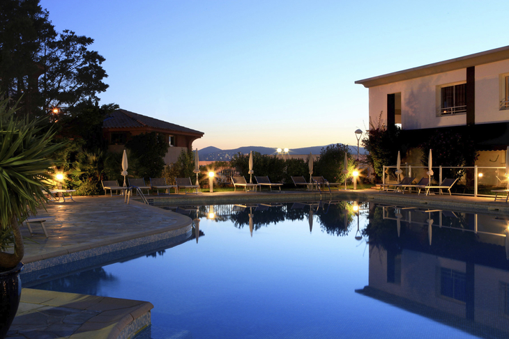 Hotelpool bei Sonnenuntergang, umgeben von Gebäuden und Pflanzen.