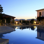 Hotelpool bei Sonnenuntergang, umgeben von Gebäuden und Pflanzen.