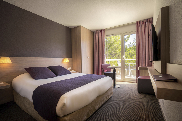 Hotelzimmer mit Doppelbett, Balkon und moderner Einrichtung.