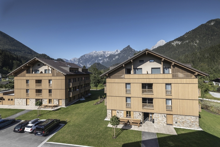 Zwei moderne Gebäude in alpiner Landschaft mit Bergen im Hintergrund.