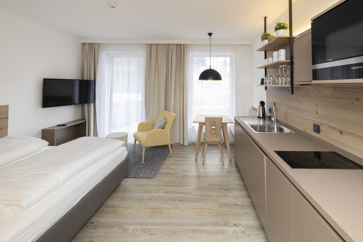 Modernes Hotelzimmer mit Doppelbett, Küchenzeile und Sitzbereich.