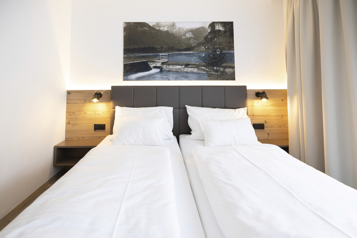 Zwei Einzelbetten in modernem Schlafzimmer mit Wandbild und Leselampen.