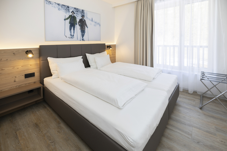 Helles Schlafzimmer mit Doppelbett, Holzwandpaneel und großem Fenster.