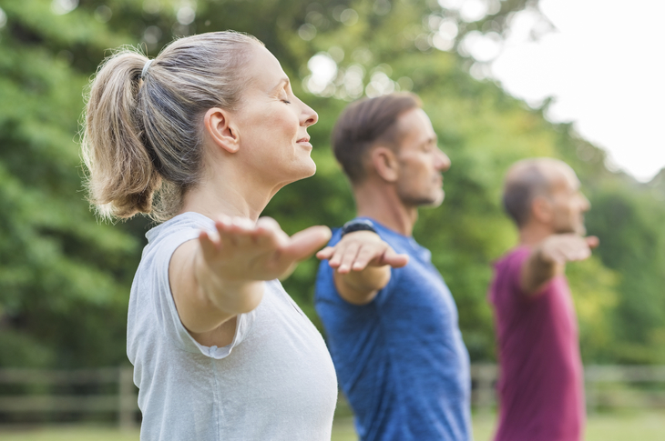Personen beim Yoga im Park, mit ausgestreckten Armen in einer Reihe stehend.