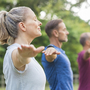Personen beim Yoga im Park, mit ausgestreckten Armen in einer Reihe stehend.