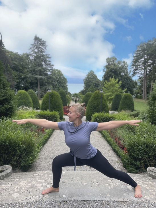 Person in Yoga-Pose im Freien, umgeben von Bäumen und gepflegtem Garten.